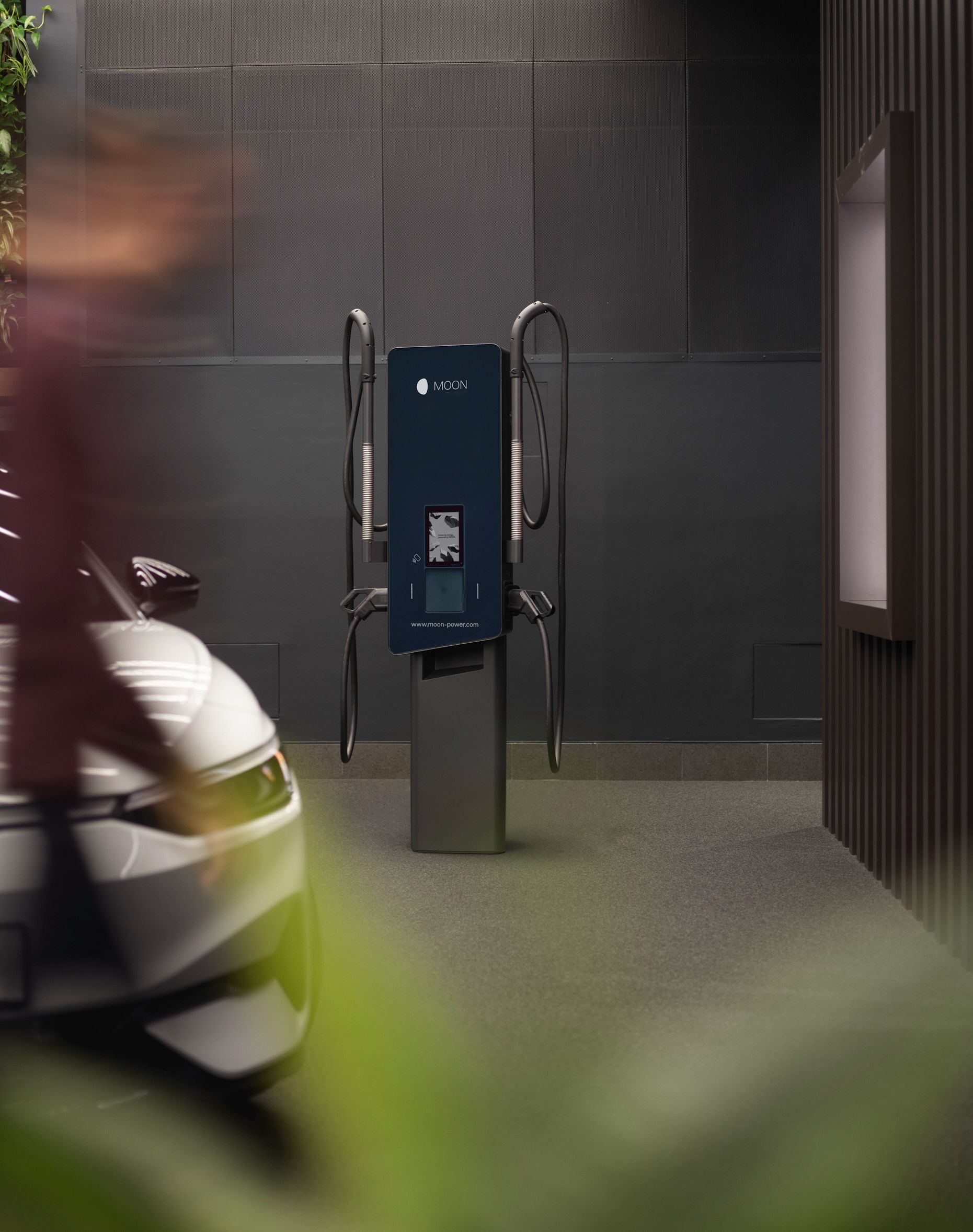 Töltőállomás egy szürke fal előtt, autóval az előtérben