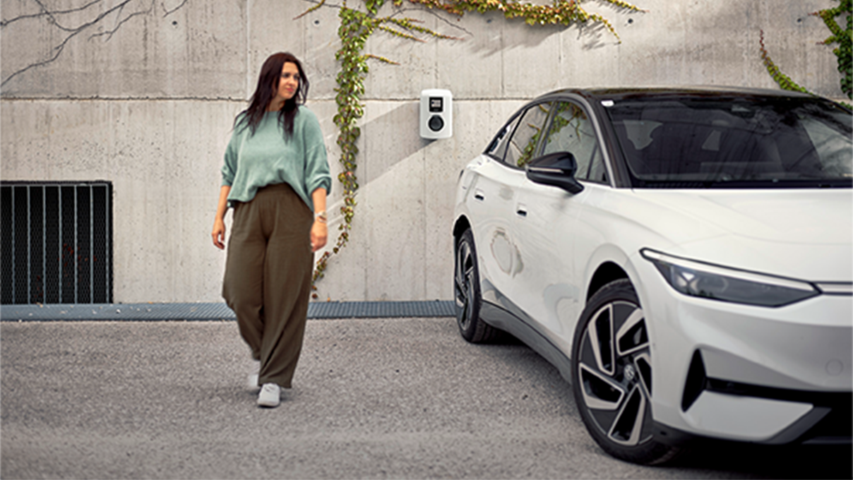 Nő egy autó mellett sétál a kamera felé