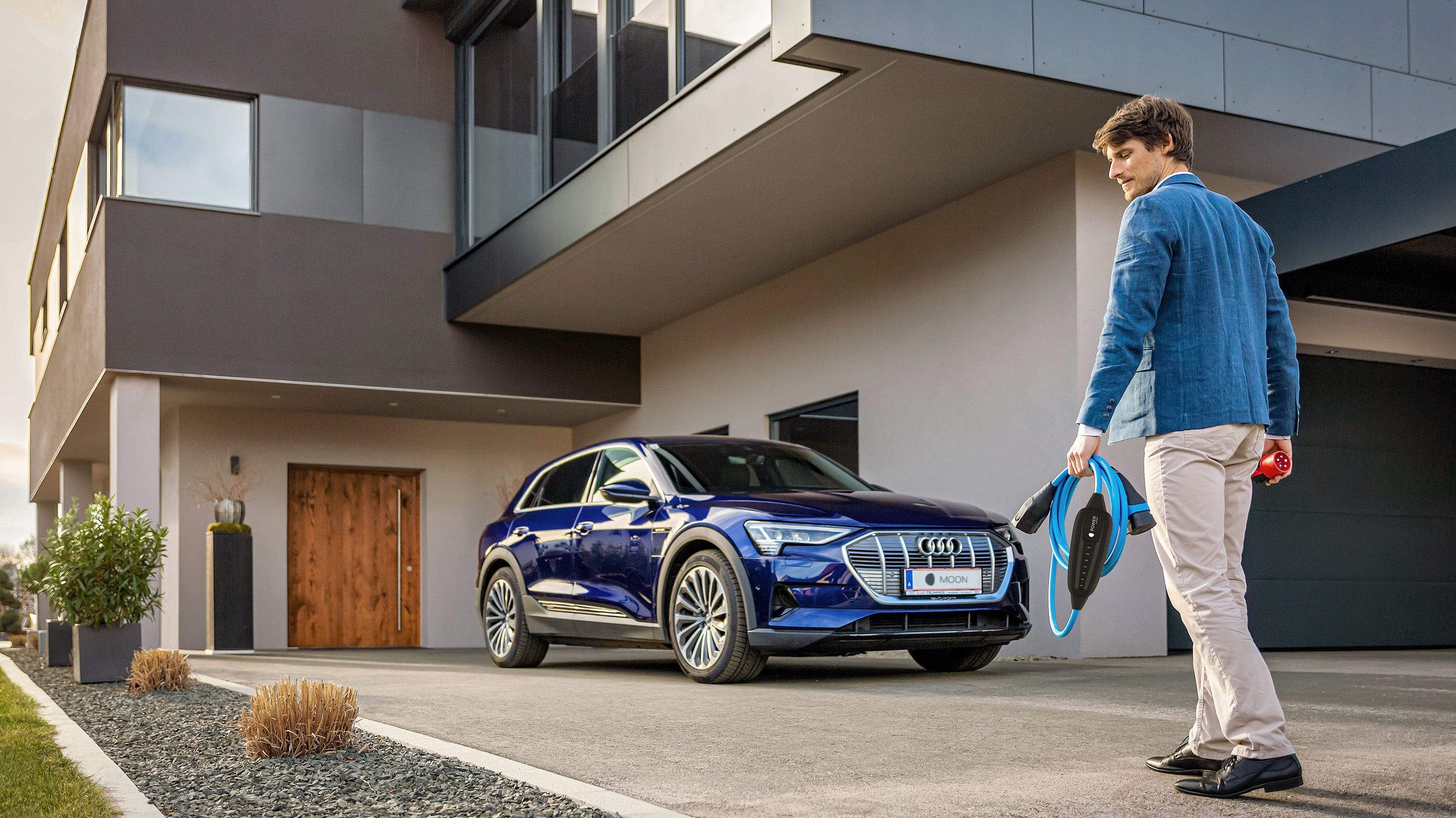 Férfi egy ház közelében lévő autó felé sétál, kezében kábellel