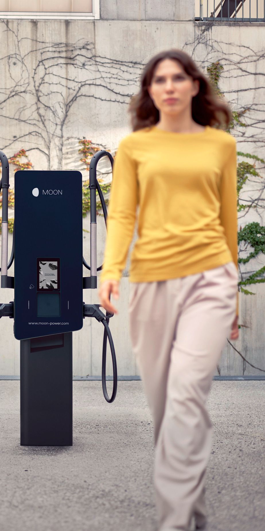 Egy nő egy töltőállomás előtt sétál, háttérben egy autóval