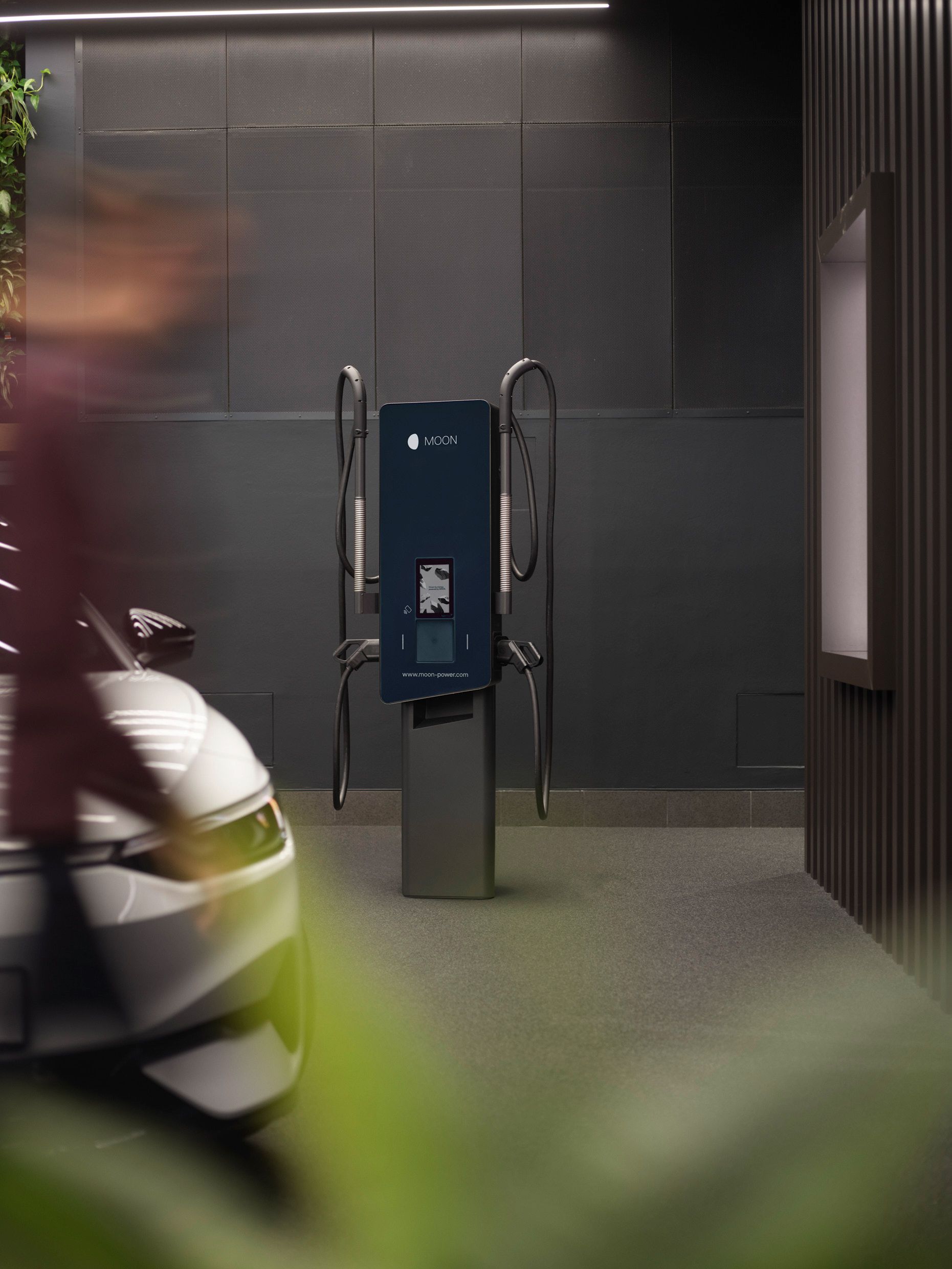Töltőállomás egy szürke falú szobában, előtérben egy autó
